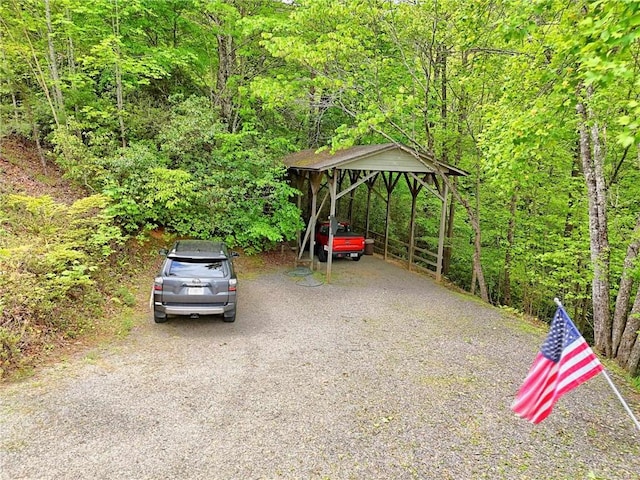 view of parking featuring a detached carport, driveway, and a forest view