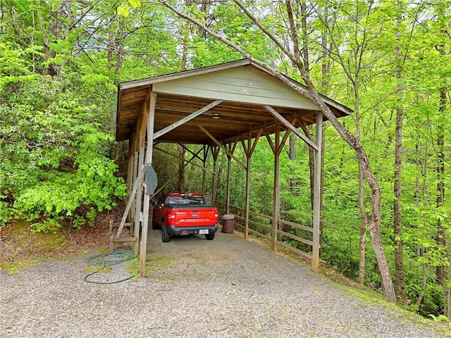 view of parking featuring a carport, a view of trees, and driveway