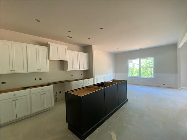 4678 Glore Rd SW, Mableton, GA 30126 - kitchen with a wainscoted wall, a kitchen island, concrete flooring, a decorative wall, and white cabinetry