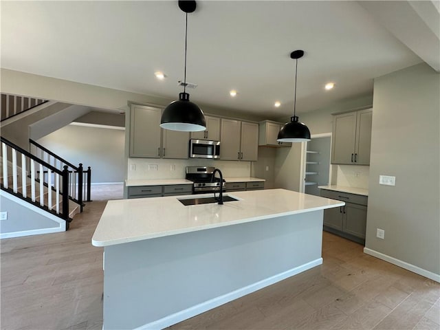 kitchen with gray cabinetry, light hardwood / wood-style flooring, a center island with sink, decorative light fixtures, and appliances with stainless steel finishes