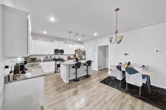 kitchen with stainless steel appliances, light wood-style floors, a breakfast bar, a center island, and hanging light fixtures