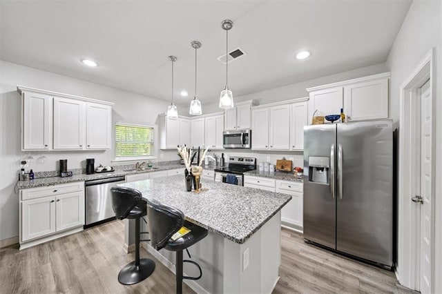 kitchen with stainless steel appliances, white cabinetry, a kitchen island, a sink, and a kitchen breakfast bar