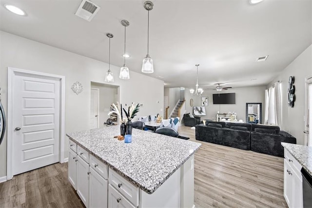 kitchen featuring wood finished floors, a ceiling fan, hanging light fixtures, white cabinets, and light stone counters