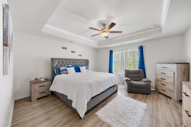 bedroom featuring a raised ceiling, light wood-style flooring, baseboards, and ceiling fan