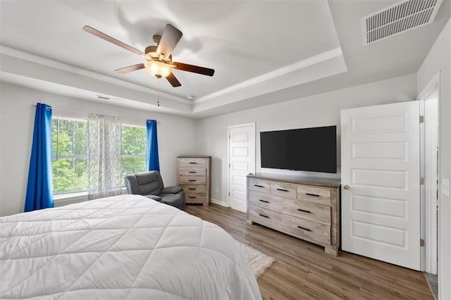 bedroom with a raised ceiling, ornamental molding, wood finished floors, ceiling fan, and baseboards