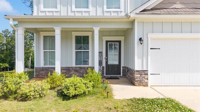 doorway to property with board and batten siding, a garage, stone siding, and a porch