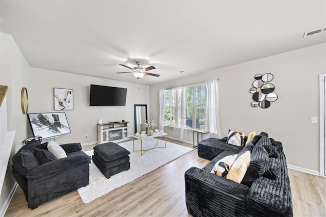 living room with baseboards, light wood-style flooring, ceiling fan, and a fireplace