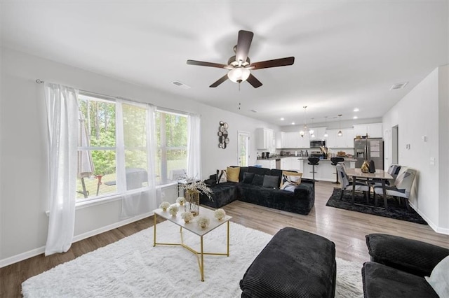 living room with ceiling fan, baseboards, and light wood-style floors