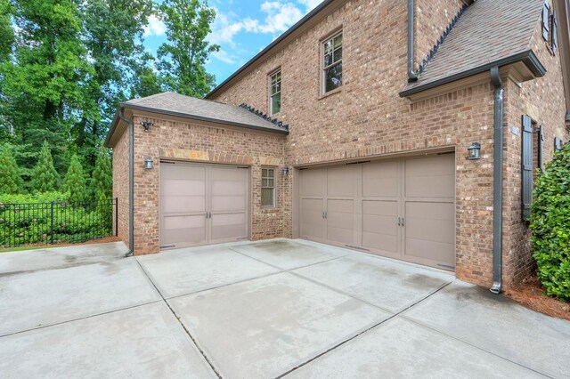 view of side of home with brick siding, fence, concrete driveway, an attached garage, and a shingled roof