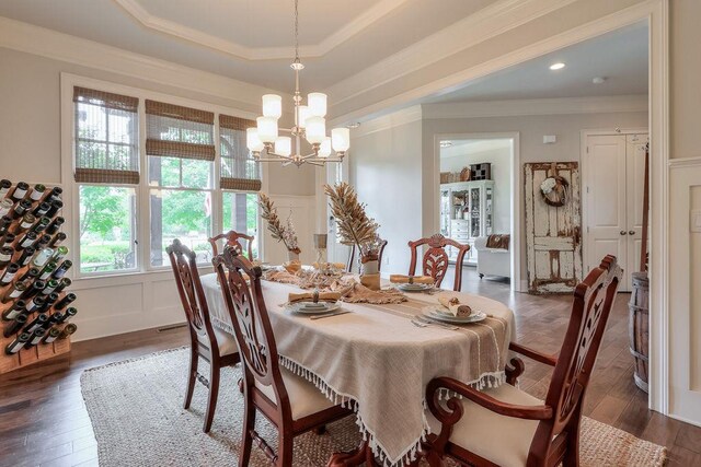 dining room with a decorative wall, wood finished floors, a notable chandelier, ornamental molding, and a tray ceiling