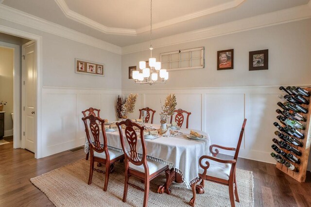 dining area with a notable chandelier, dark wood-style floors, a raised ceiling, and a decorative wall
