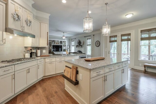 kitchen featuring stainless steel gas cooktop, dark wood-style flooring, ornamental molding, and ceiling fan with notable chandelier