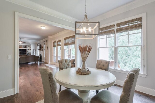 dining space featuring crown molding, dark wood-style flooring, a fireplace, baseboards, and ceiling fan with notable chandelier