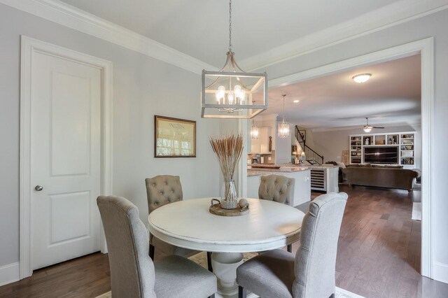 dining space with ornamental molding, ceiling fan with notable chandelier, stairs, and dark wood-style floors