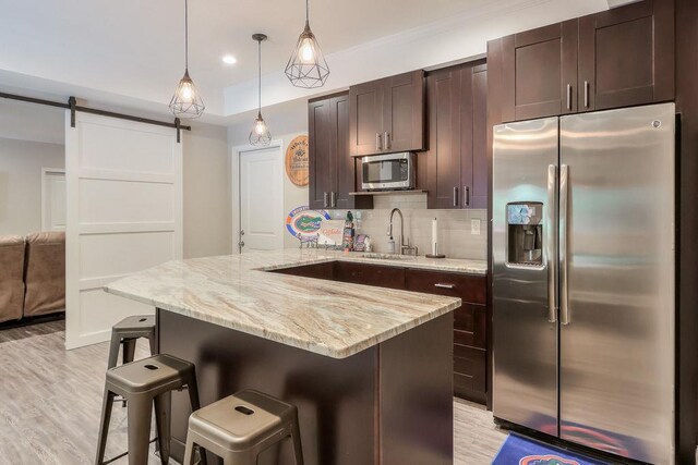 kitchen with dark brown cabinetry, appliances with stainless steel finishes, a sink, a kitchen breakfast bar, and light wood-style flooring