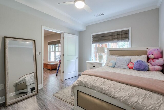 bedroom with crown molding, ceiling fan, baseboards, wood finished floors, and visible vents