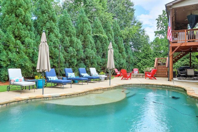 outdoor pool with stairway, a fire pit, a patio area, and a wooden deck