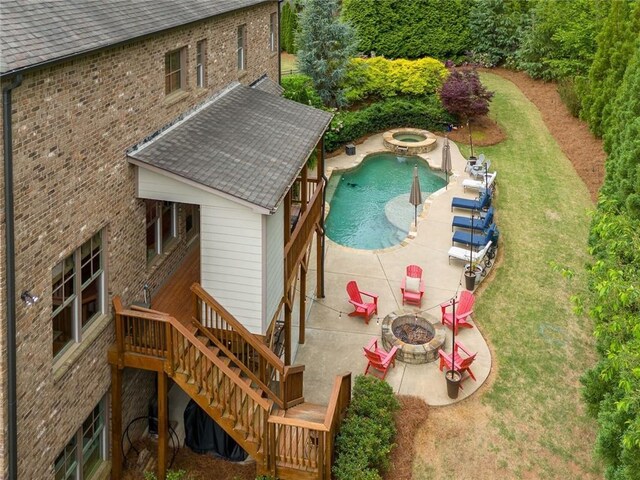 rear view of property with a shingled roof, stairway, an in ground hot tub, a patio area, and a fire pit