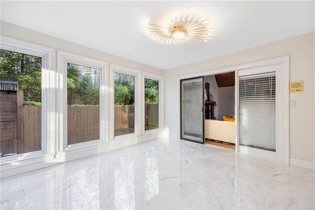 empty room with marble finish floor, plenty of natural light, and baseboards