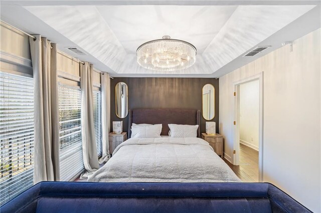 bedroom with a chandelier, visible vents, baseboards, light wood finished floors, and a raised ceiling