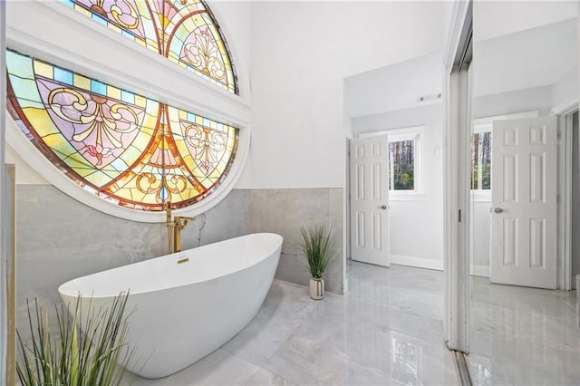 bathroom with marble finish floor, a freestanding bath, and tile walls