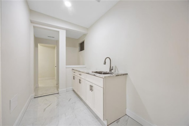 interior space with marble finish floor, white cabinets, a sink, and baseboards