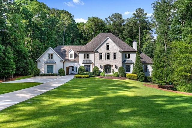 view of front of property with stone siding, a standing seam roof, concrete driveway, and a front yard
