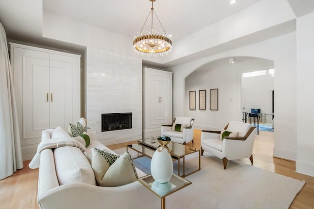 living area featuring arched walkways, a chandelier, a fireplace, light wood-type flooring, and baseboards