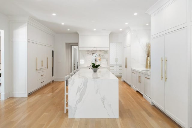 kitchen featuring backsplash, a center island, light wood-style flooring, light stone countertops, and white cabinets