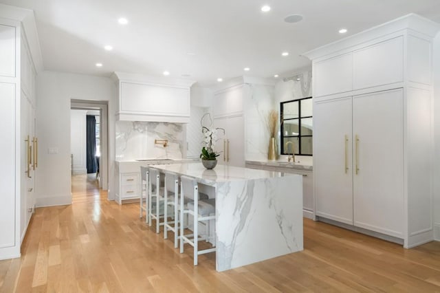 kitchen with tasteful backsplash, white cabinets, light wood finished floors, recessed lighting, and a kitchen island