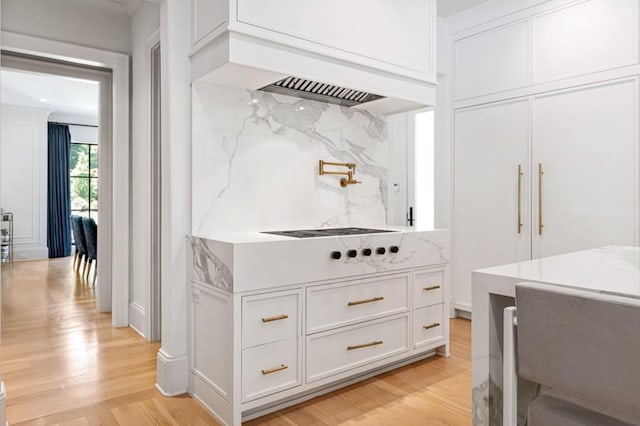 kitchen featuring white cabinetry, light wood-style flooring, cooktop, decorative backsplash, and light stone countertops