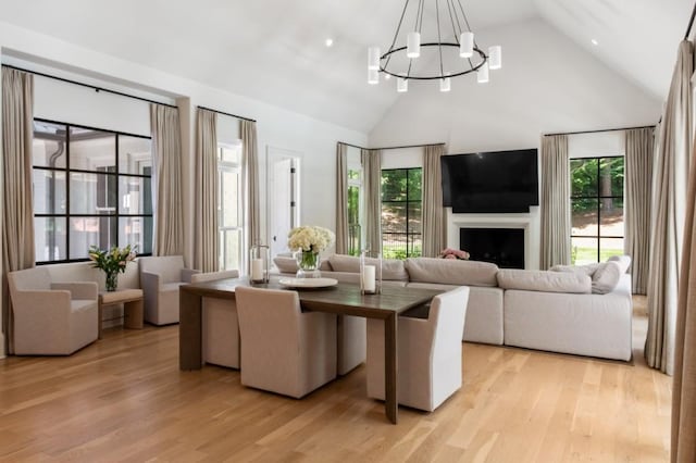 dining area featuring high vaulted ceiling, a chandelier, light wood-style floors, and a fireplace