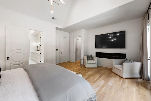 bedroom featuring light wood-style flooring, baseboards, high vaulted ceiling, and connected bathroom