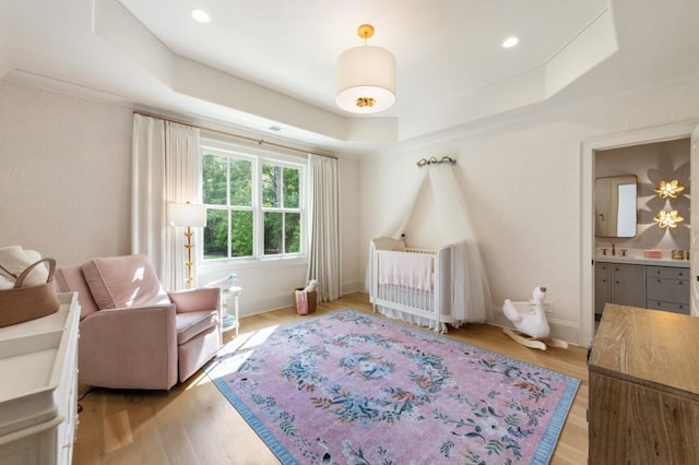 bedroom featuring a raised ceiling, light wood finished floors, baseboards, ensuite bath, and recessed lighting