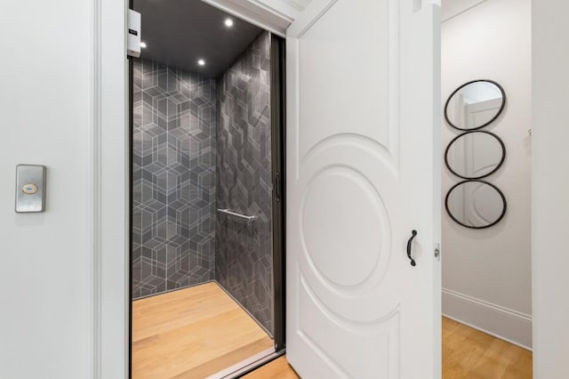 bathroom featuring elevator, a tile shower, baseboards, wood finished floors, and recessed lighting