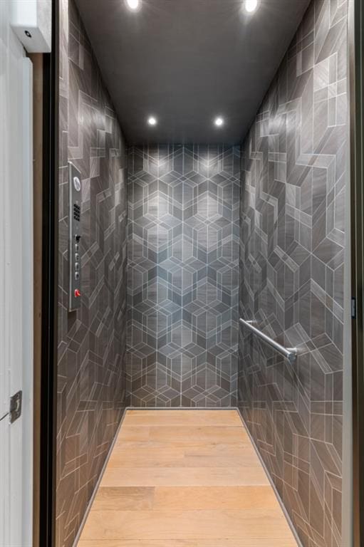 full bathroom featuring recessed lighting, tiled shower, elevator, and wood finished floors