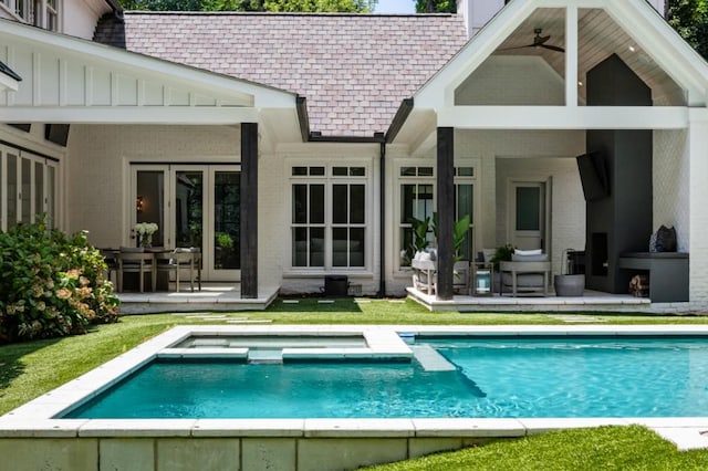 back of house with a ceiling fan, a pool with connected hot tub, brick siding, a patio area, and roof with shingles