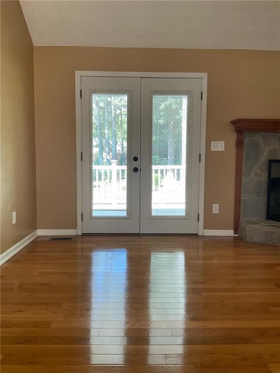 doorway with french doors, a stone fireplace, a textured ceiling, and wood-type flooring