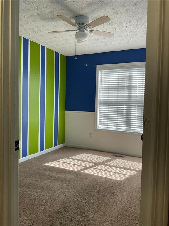 unfurnished room featuring a textured ceiling, carpet flooring, and ceiling fan