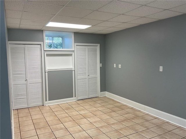 unfurnished bedroom featuring a paneled ceiling, light tile patterned flooring, and two closets