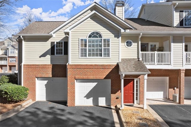 townhome / multi-family property with brick siding, an attached garage, a shingled roof, a chimney, and driveway