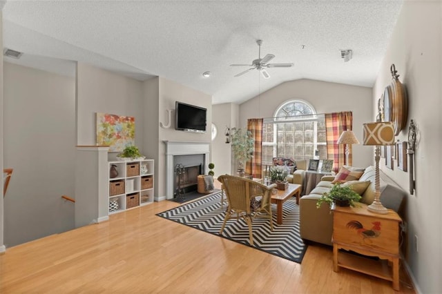 living area featuring visible vents, a fireplace with flush hearth, lofted ceiling, wood finished floors, and a textured ceiling