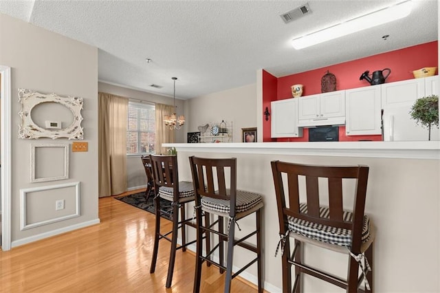 kitchen with visible vents, under cabinet range hood, light wood-style flooring, a kitchen breakfast bar, and white cabinetry