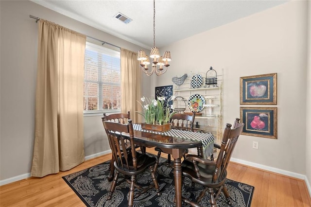 dining room with a chandelier, baseboards, visible vents, and wood finished floors