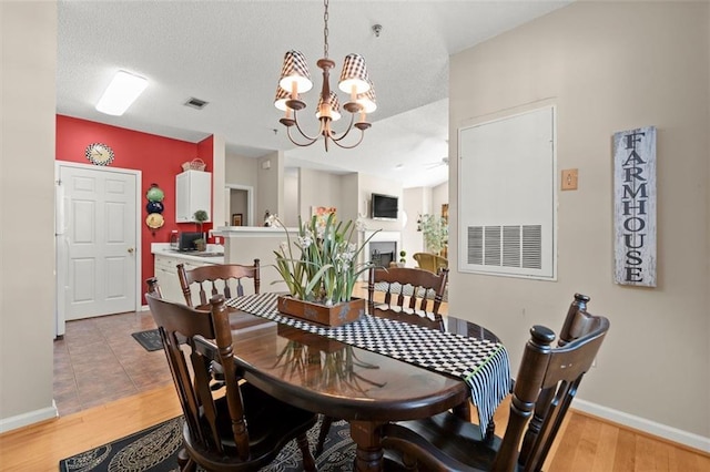 dining room featuring light wood-type flooring, visible vents, a textured ceiling, a fireplace, and baseboards