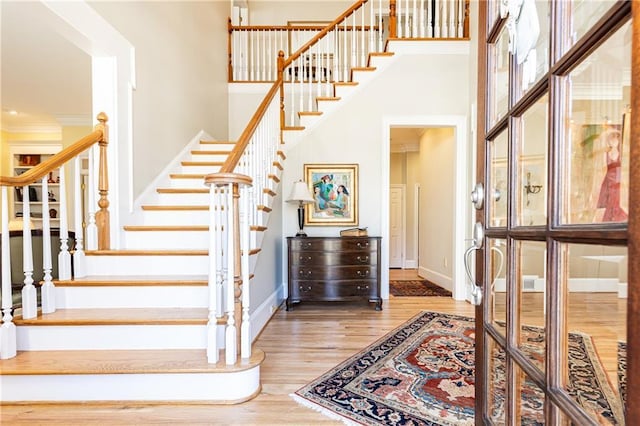 staircase featuring ornamental molding, a towering ceiling, and hardwood / wood-style floors