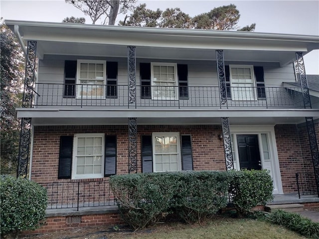 view of front of house featuring covered porch, brick siding, and a balcony