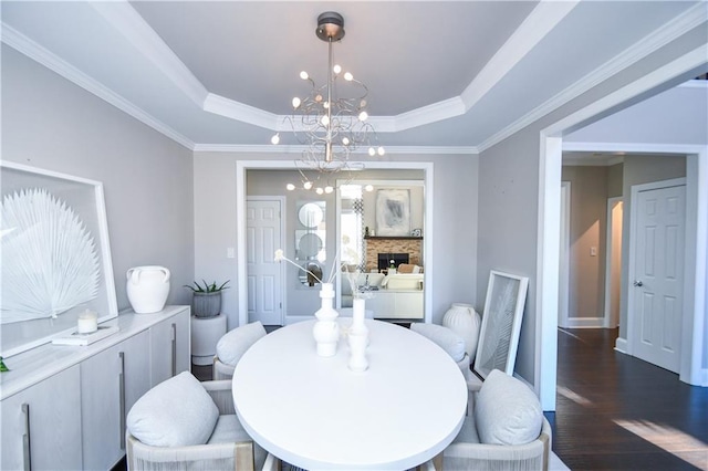 dining area with a raised ceiling, dark hardwood / wood-style flooring, ornamental molding, and a notable chandelier