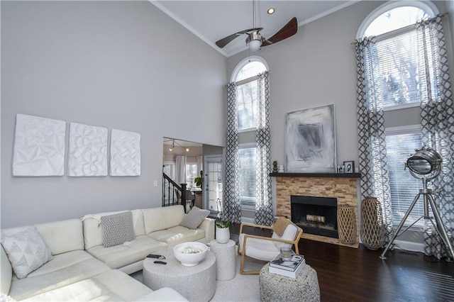 living room with a high ceiling, dark hardwood / wood-style floors, a stone fireplace, and crown molding