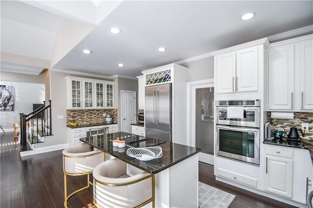 kitchen featuring decorative backsplash, dark stone counters, stainless steel appliances, white cabinets, and a kitchen island